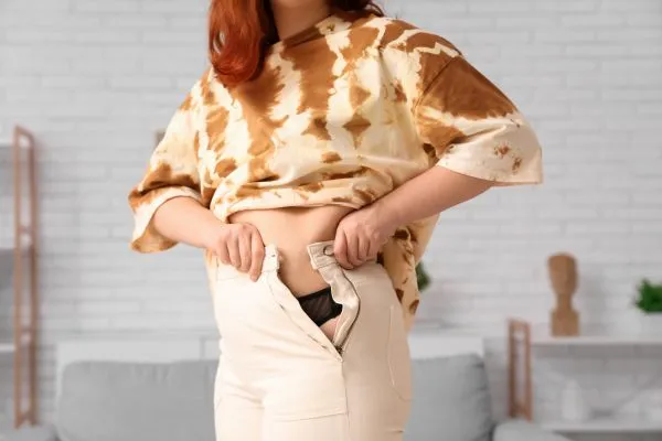 Image of woman trying to do her trousers up after pregnancy weight gain Orrell